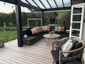 Une terrasse extérieure dotée d’un espace salon couvert, d’une table ronde et d’un fauteuil en osier.