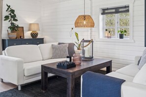 Une pièce avec un canapé blanc, une table basse en bois foncé, une lampe en osier et une fenêtre donnant sur des arbres.