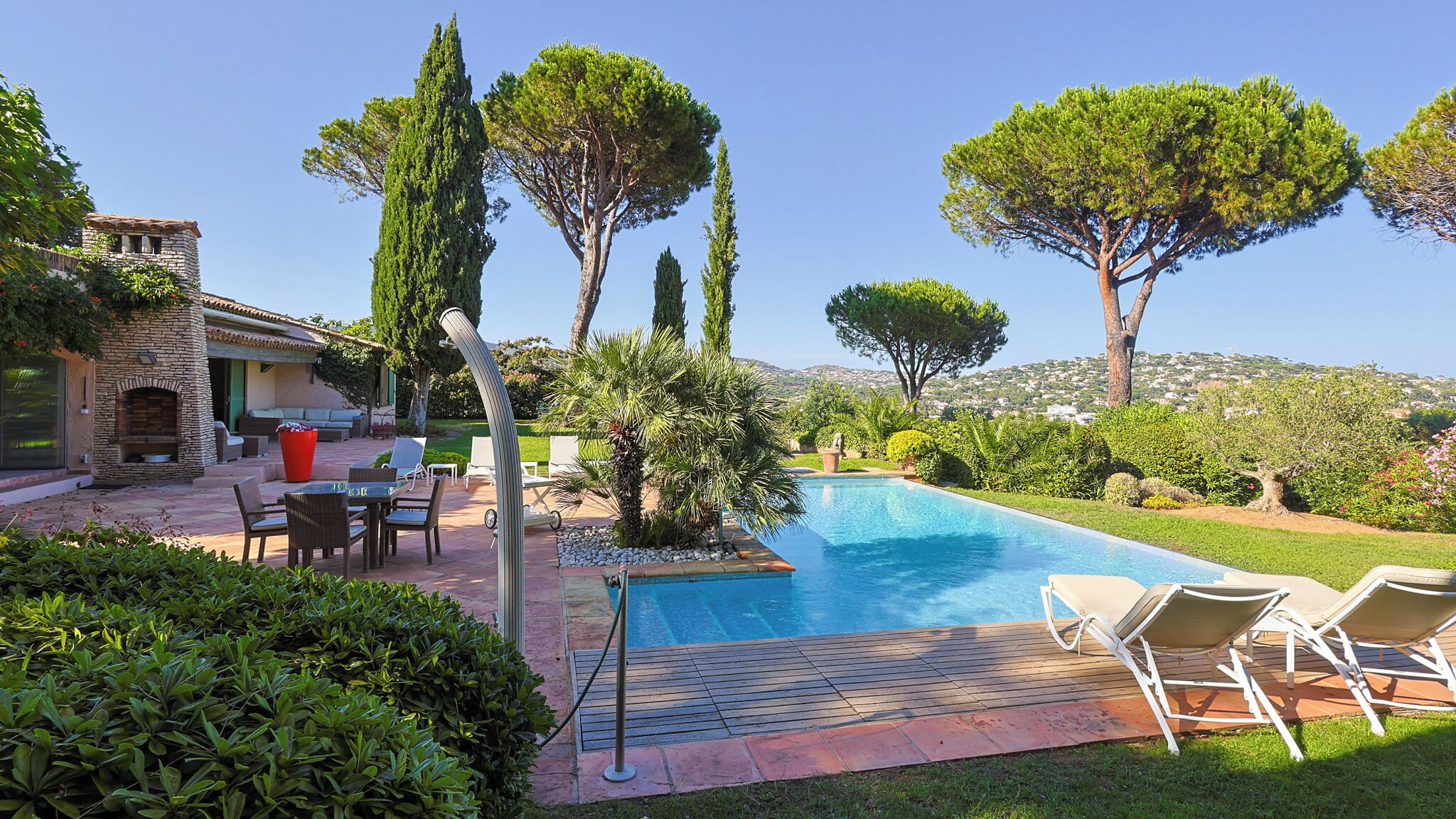 A poolside area with a stone fireplace, outdoor seating, and a view of the surrounding landscape.