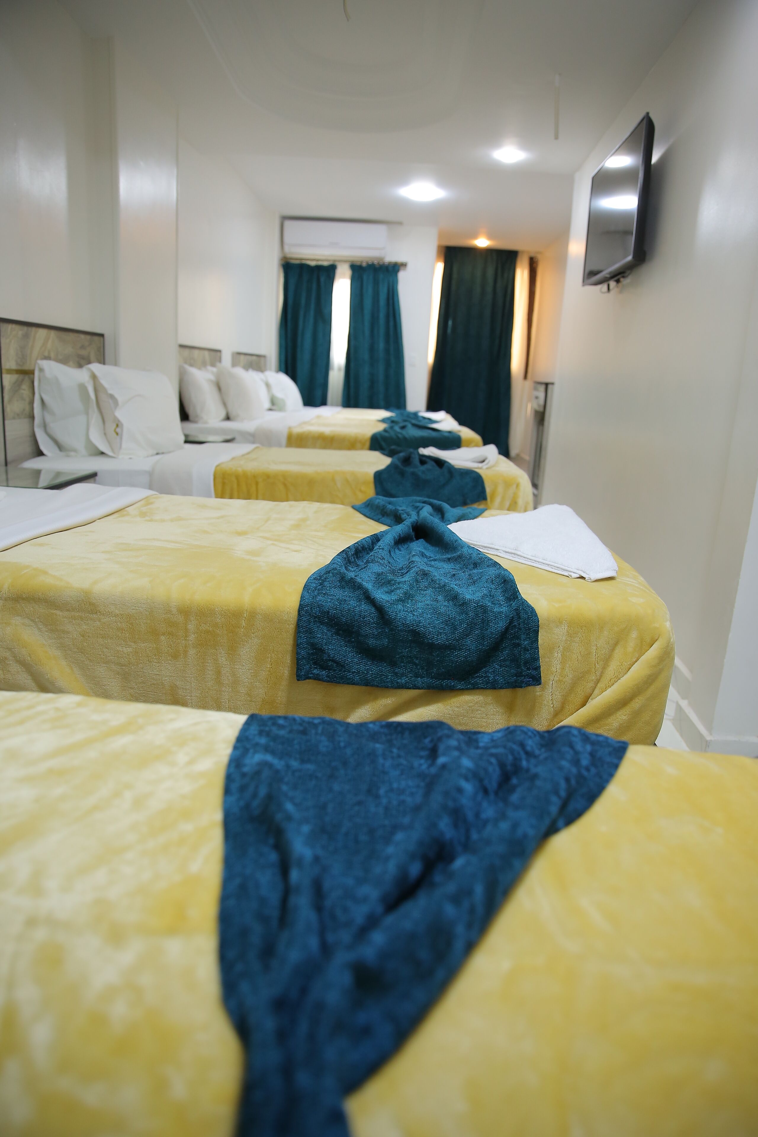 Une chambre d’hôtel avec quatre lits, chacun recouvert d’une couverture jaune et agrémenté d’une serviette bleue.