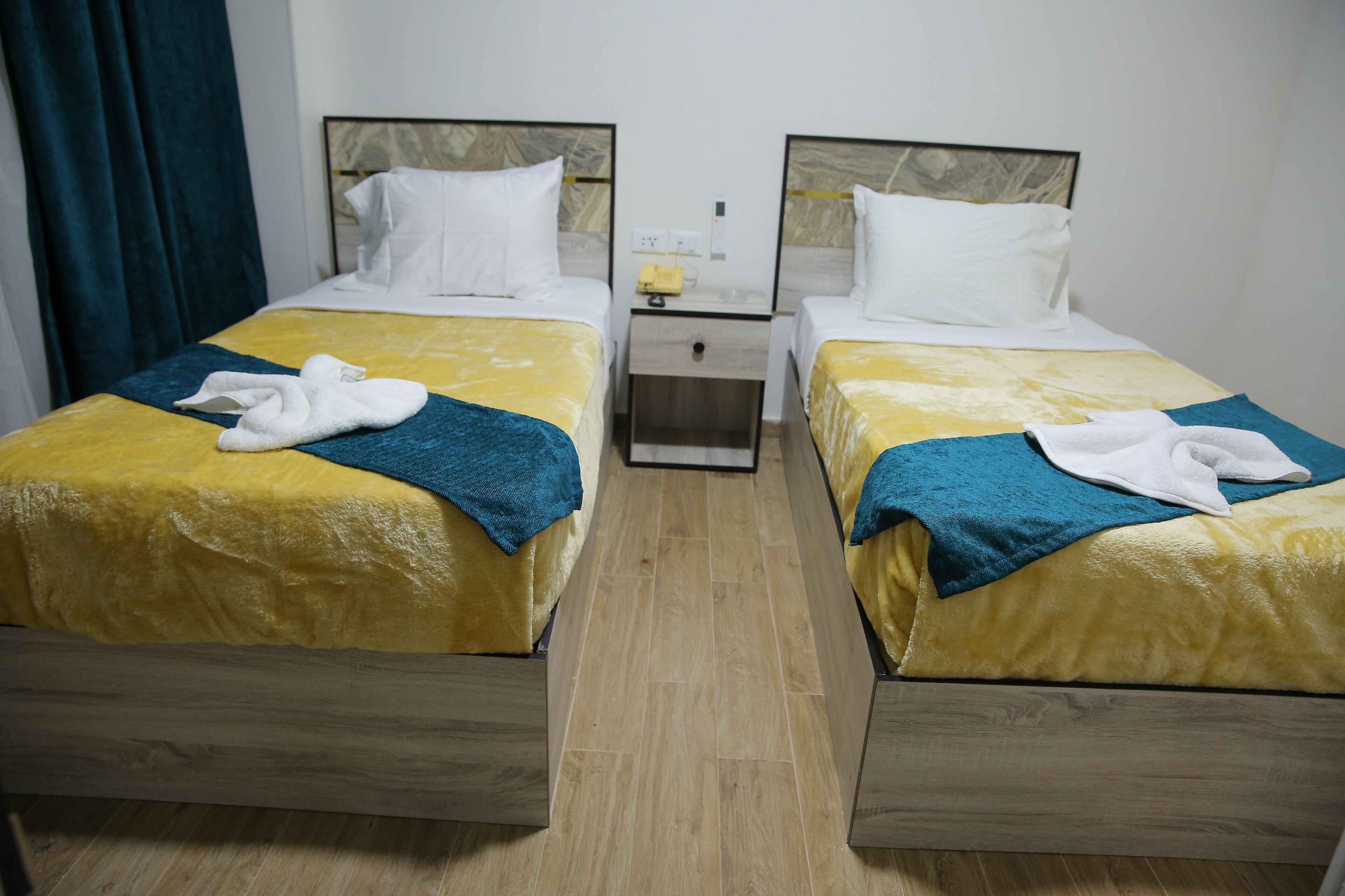 A hotel room with two beds, each with a wooden frame and yellow bedding. There are towels on the beds and a nightstand between them.