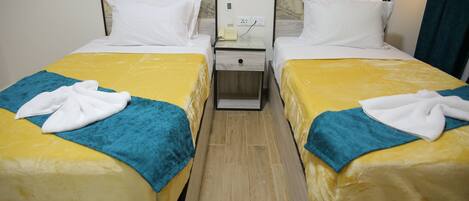 A hotel room with two beds, each with a yellow and blue bedspread, white pillows, and a white bathrobe on the bed. There is a nightstand with a phone and a power outlet between the beds.