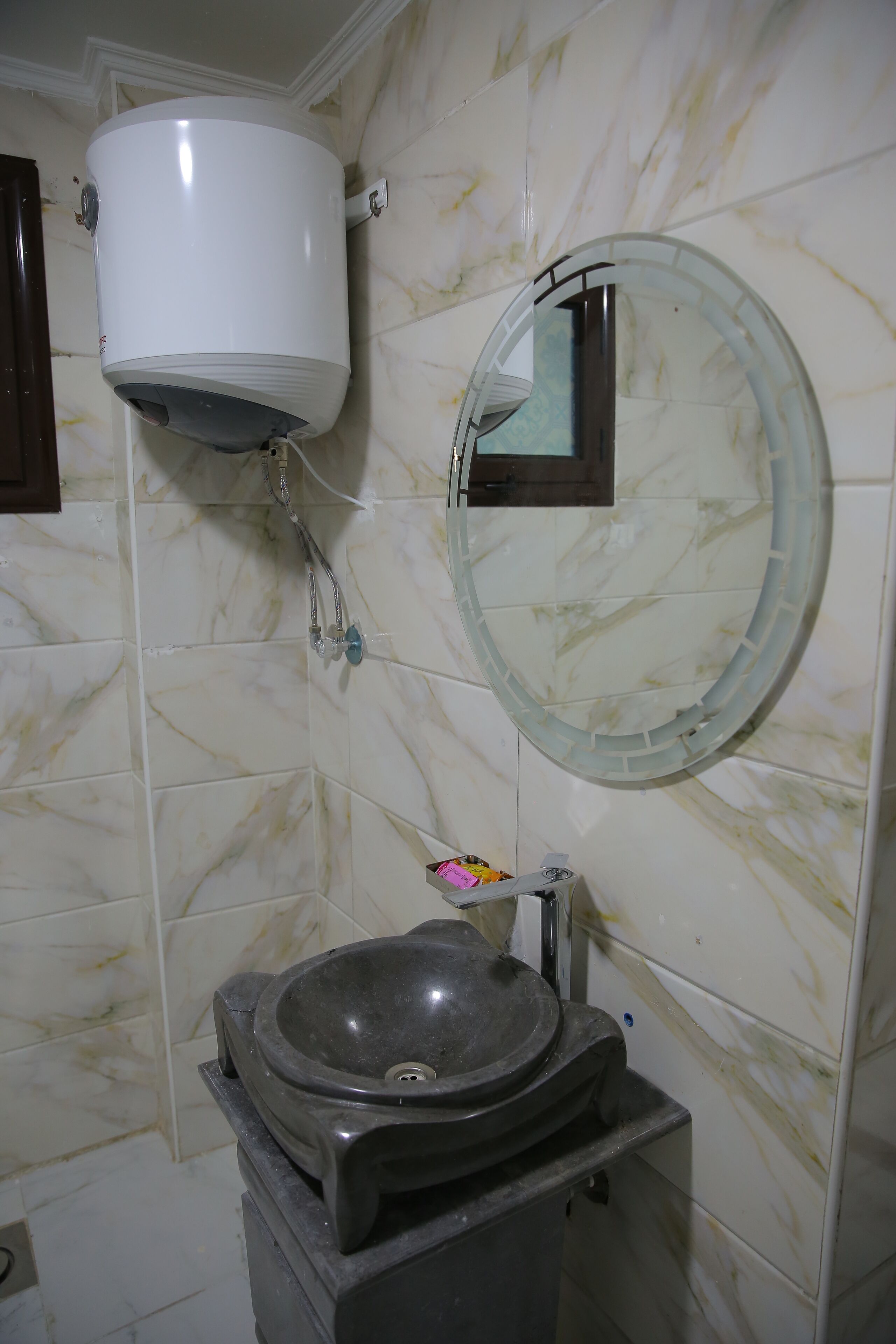 A bathroom with a marble-tiled wall, a round mirror, a pedestal sink, and a toilet tank.