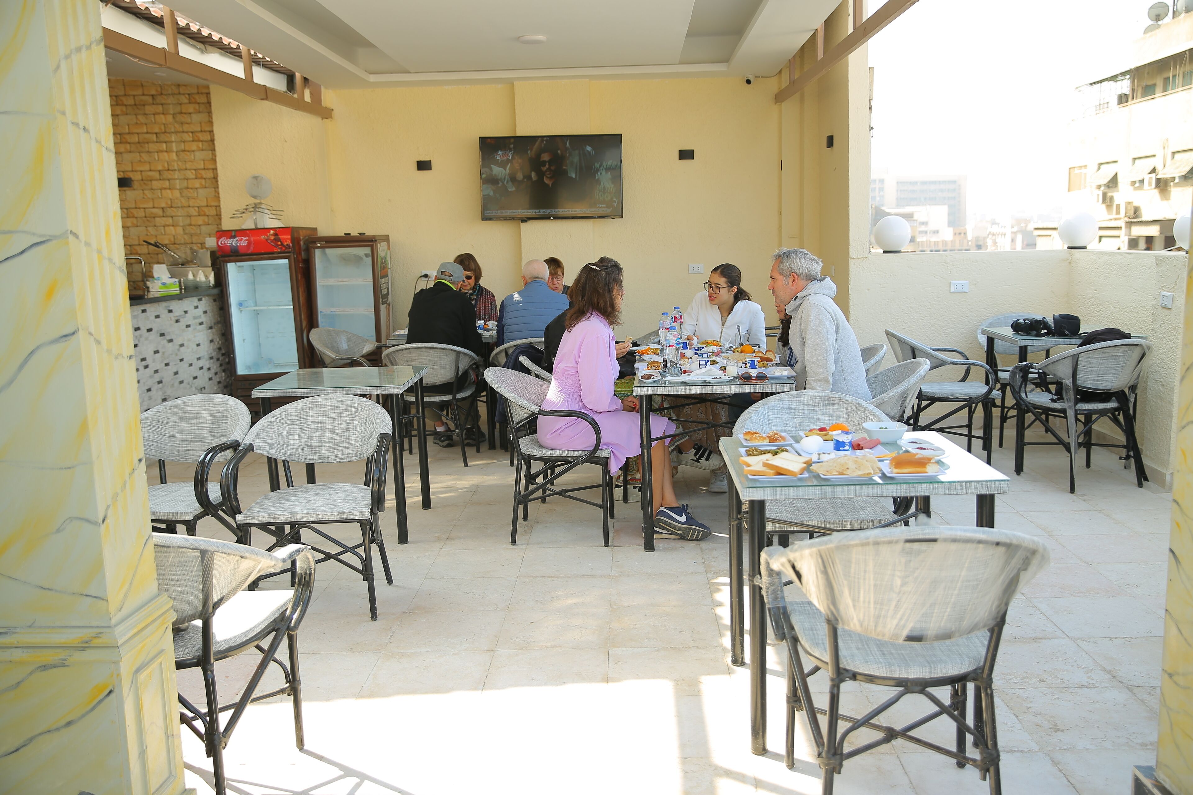 An outdoor dining area with wicker chairs and tables, a refrigerator, and a television mounted on the wall.