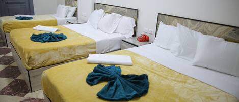 A hotel room with three beds, each with a yellow bedspread and white pillows. There is a telephone on the nightstand and a door in the background.