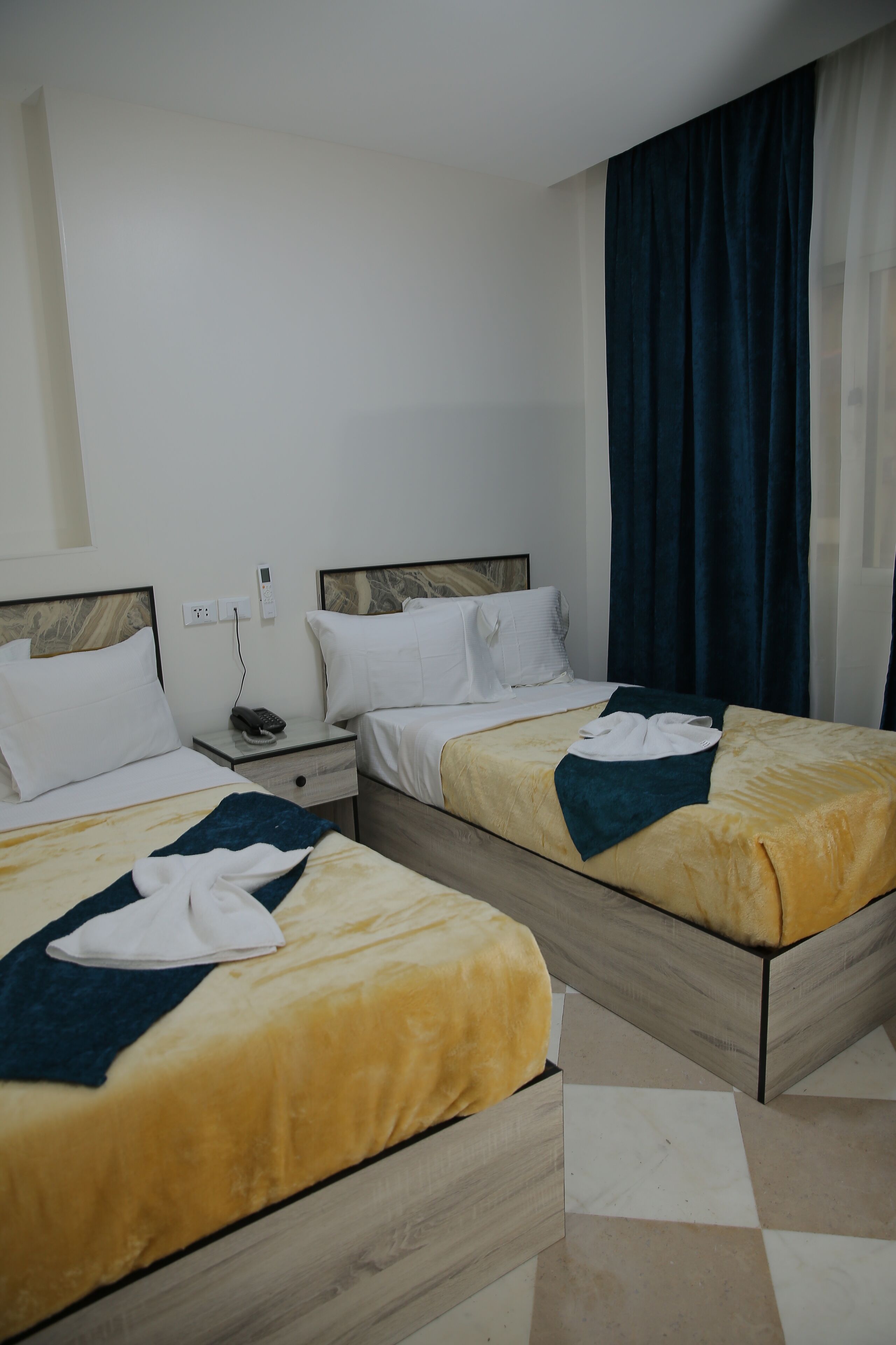 Une chambre d’hôtel avec deux lits, une table de chevet et une grande fenêtre avec des rideaux.