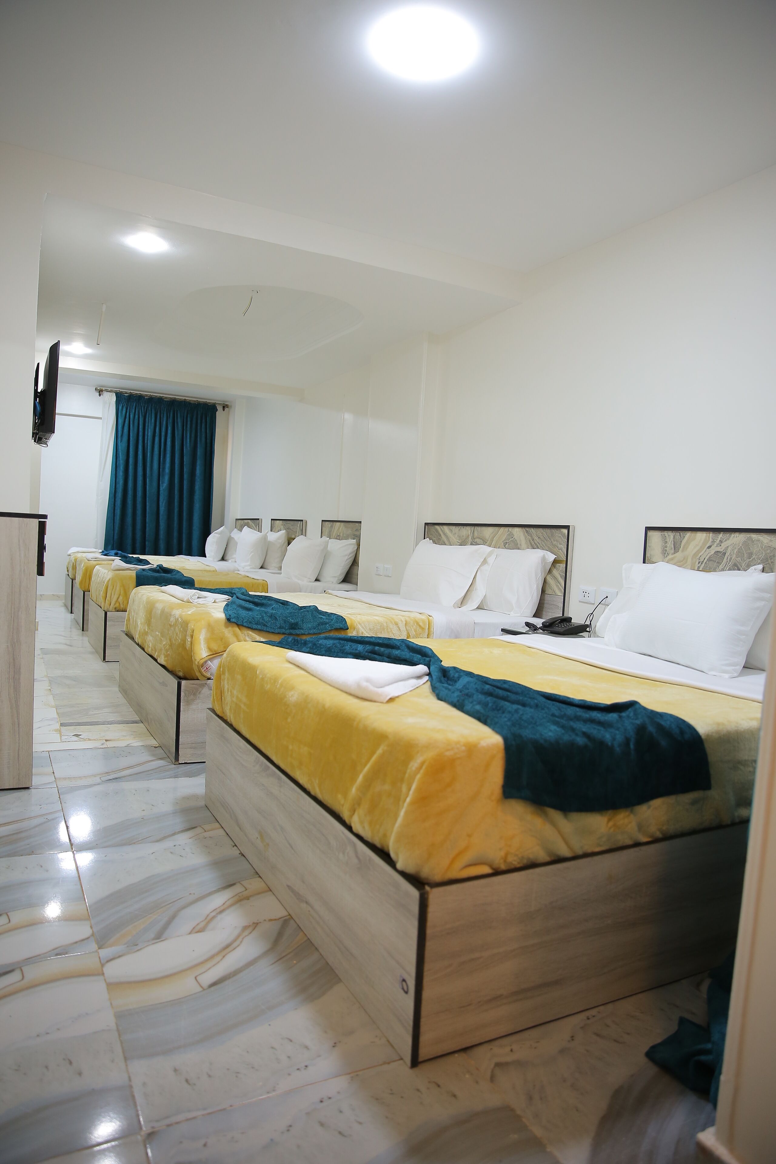 A hotel room with four beds aligned in a row, each with a wooden frame and white bedding.