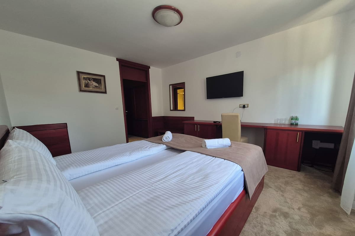 A hotel room with two beds, a desk, a chair, a television, and a door leading to a bathroom.