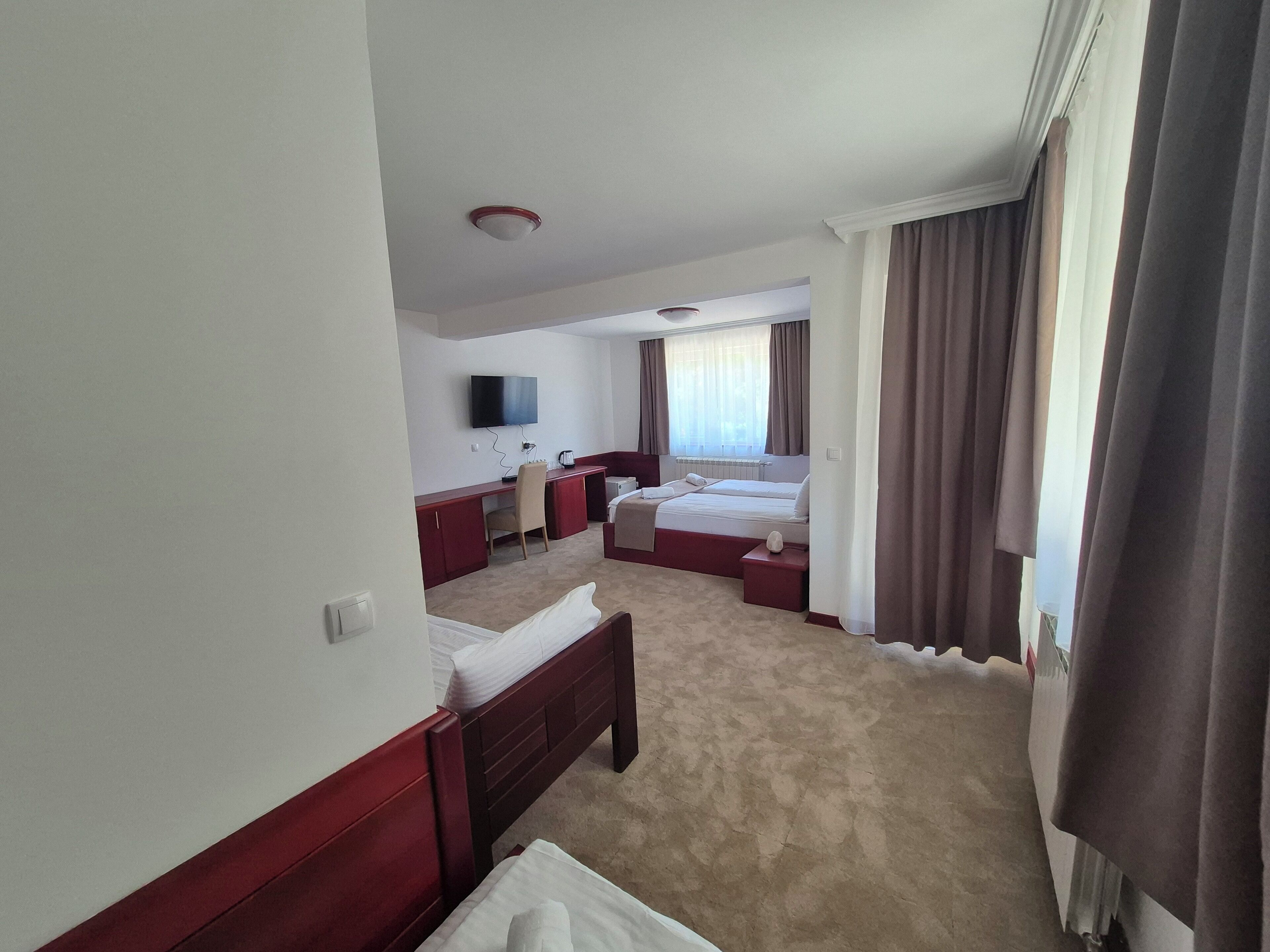 A hotel room with a large bed, a smaller bed, a desk with a chair, a television, and a window with curtains.