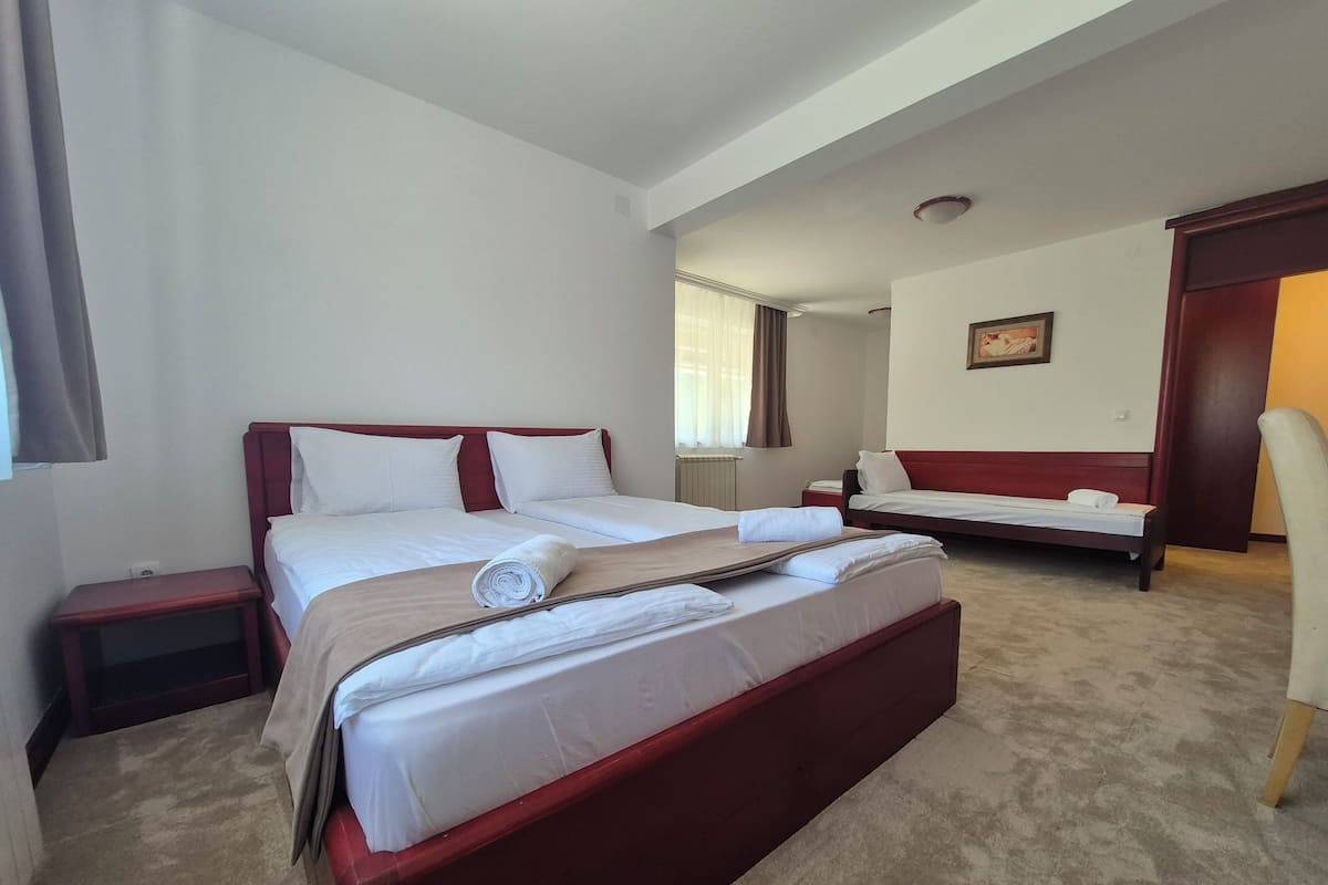 A hotel room with a large bed, a smaller bed, a chair, a nightstand, and a painting on the wall.