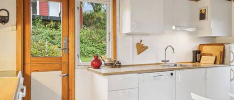 A compact kitchen with white cabinets, a wooden countertop, a window with a view of greenery, and a small refrigerator.