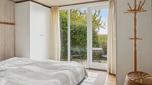 Een slaapkamer met een bed, een schuifpui naar een tuin, een houten kapstok en een rieten stoel.