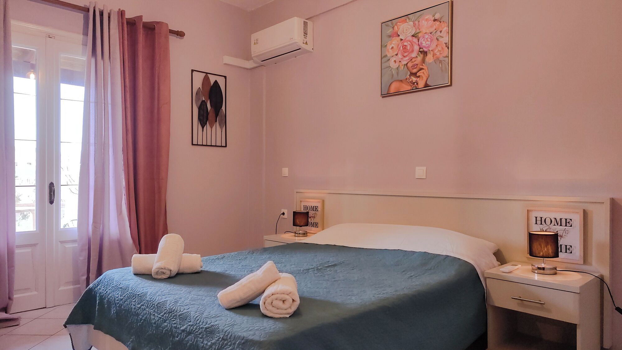 Ein Schlafzimmer mit einem Bett, zwei Nachttischen, einer Wandleuchte und einer Klimaanlage, sowie einer mit Vorhängen versehenen Tür.