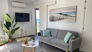 En moderne stue med en grå sofa, et fladskærms-tv, et billede af en strand og en stor plante.