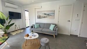 En moderne stue med en grå sofa, et rundt sofabord, et fjernsyn ophængt på væggen og en stor plantepotte.