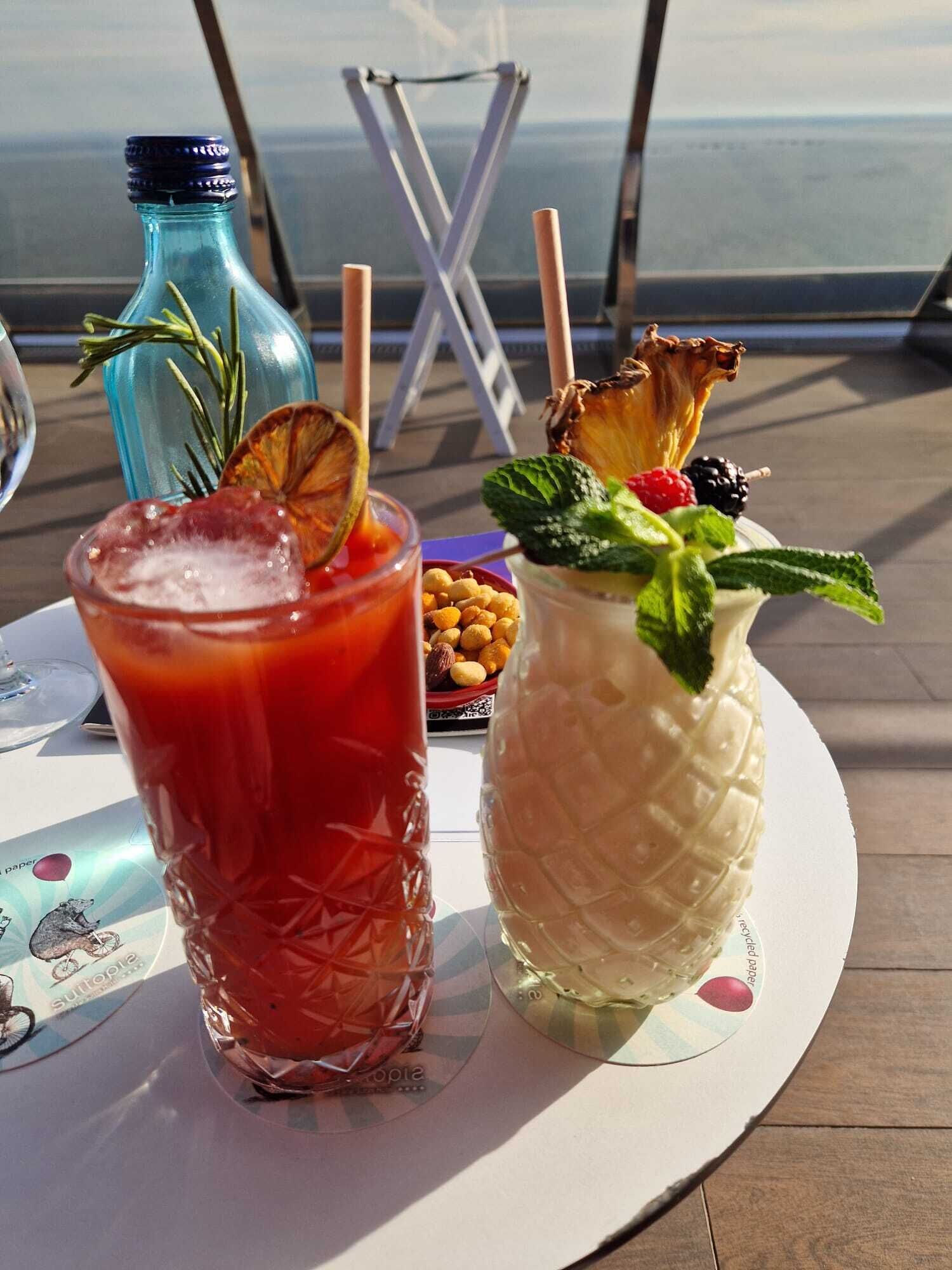 Two drinks on a table with a view of the ocean.