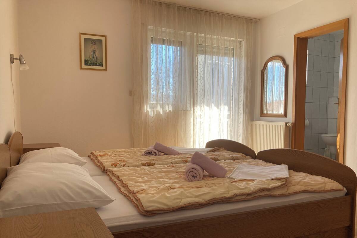 A neatly made bed with a floral-patterned duvet, a wooden headboard, and a bedside table with a lamp.