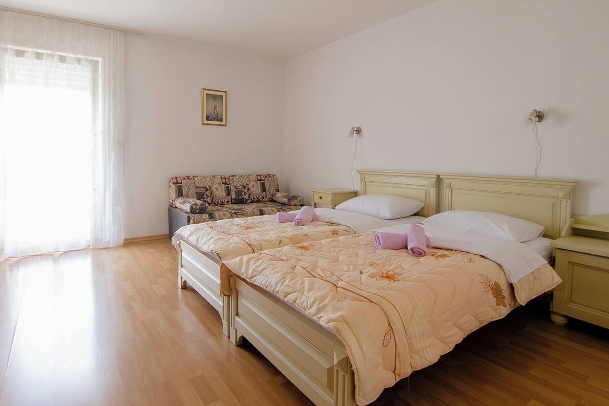 A bedroom with a double bed, a nightstand, a bedside table, a sofa, and a window with curtains.