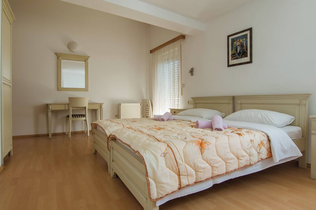 A bedroom with a bed, a desk, a chair, a mirror, and a window with curtains.