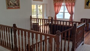 A spacious room with a wooden staircase, a dining area with a table and chairs, and a window with curtains.
