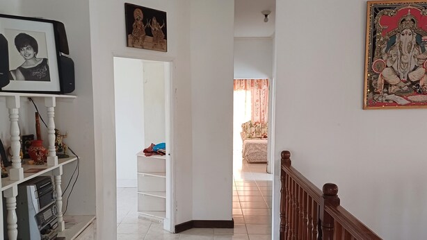 A hallway with a staircase, a door leading to a room with a floral curtain, and a shelf with various items.