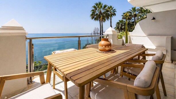 A wooden table with chairs and a vase on an outdoor balcony overlooking the sea. - Apartment on the beachfront in Estepona, (Estepona)