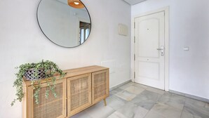 A hallway with a round mirror, a wooden cabinet with a plant, and a white door. - Apartment on the beachfront in Estepona, (Estepona)