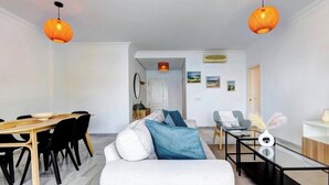 A modern living room with a white sofa, a dining table with chairs, and two hanging orange lamps. - Apartment on the beachfront in Estepona, (Estepona)