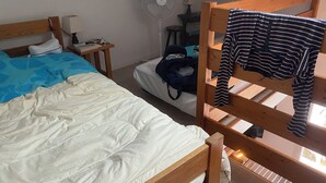 A dormitory room with two bunk beds, a desk, a chair, a lamp, a fan, and a suitcase. - Vacation home located 300m from the beach (Dolus-d'Oléron)