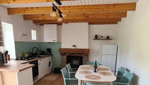 A spacious kitchen with a dining area, wooden beams, and a fireplace. - Atypical house at the entrance to Paimpol (Kerfot)