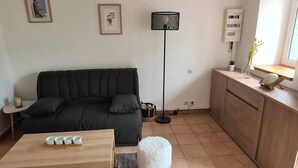 A cozy living room with a wooden ceiling, a dark green sofa, a wooden coffee table, and a white fluffy dog. - Atypical house at the entrance to Paimpol (Kerfot)