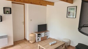 A spacious living area with a wooden ceiling, a television on a wooden stand, a green sofa, and a small white stool. - Atypical house at the entrance to Paimpol (Kerfot)