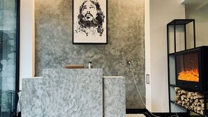 A modern living room with a grey marble reception desk, a framed artwork above it, a fireplace with logs, and a glass door leading outside. - Ben Ben Hotel (Xuan Huong - Da Lat)