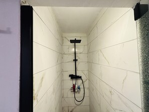 Une petite salle de douche carrelée, équipée d’un pommeau de douche à main et d’un robinet à main.