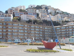 A multi-story residential building with balconies, a roundabout with a red sculpture, and a street sign indicating a no-entry zone.