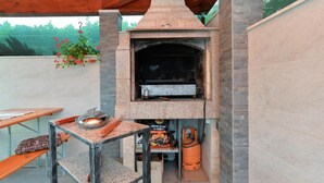 Un área de cocina al aire libre con horno de piedra, un cilindro de gas y una mesa con un tazón y una botella.