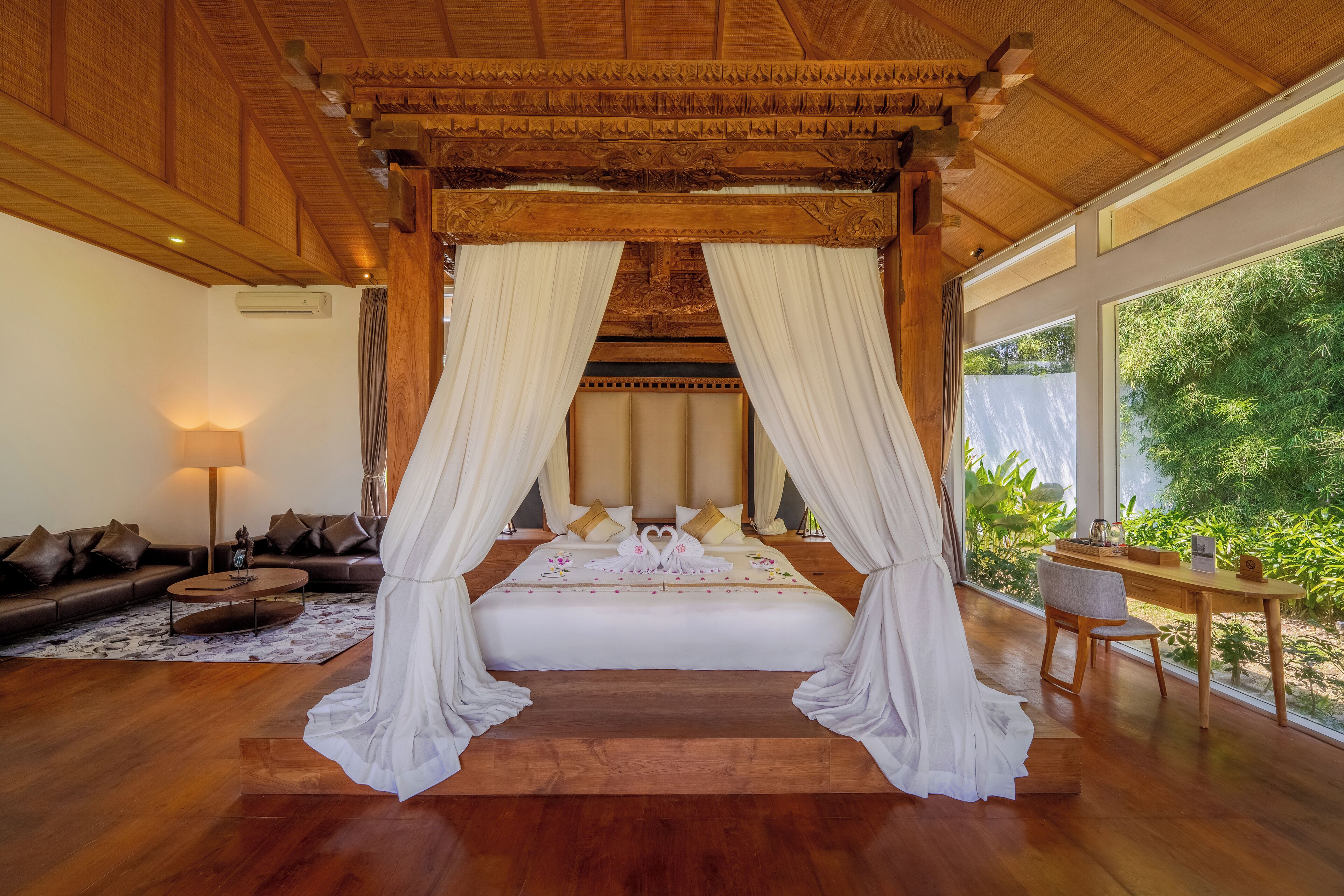 A spacious bedroom with a large bed, wooden ceiling, and a view of greenery outside.