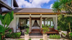 Un dormitorio moderno al aire libre con terraza de madera, cama con dosel y jardín con plantas en macetas.