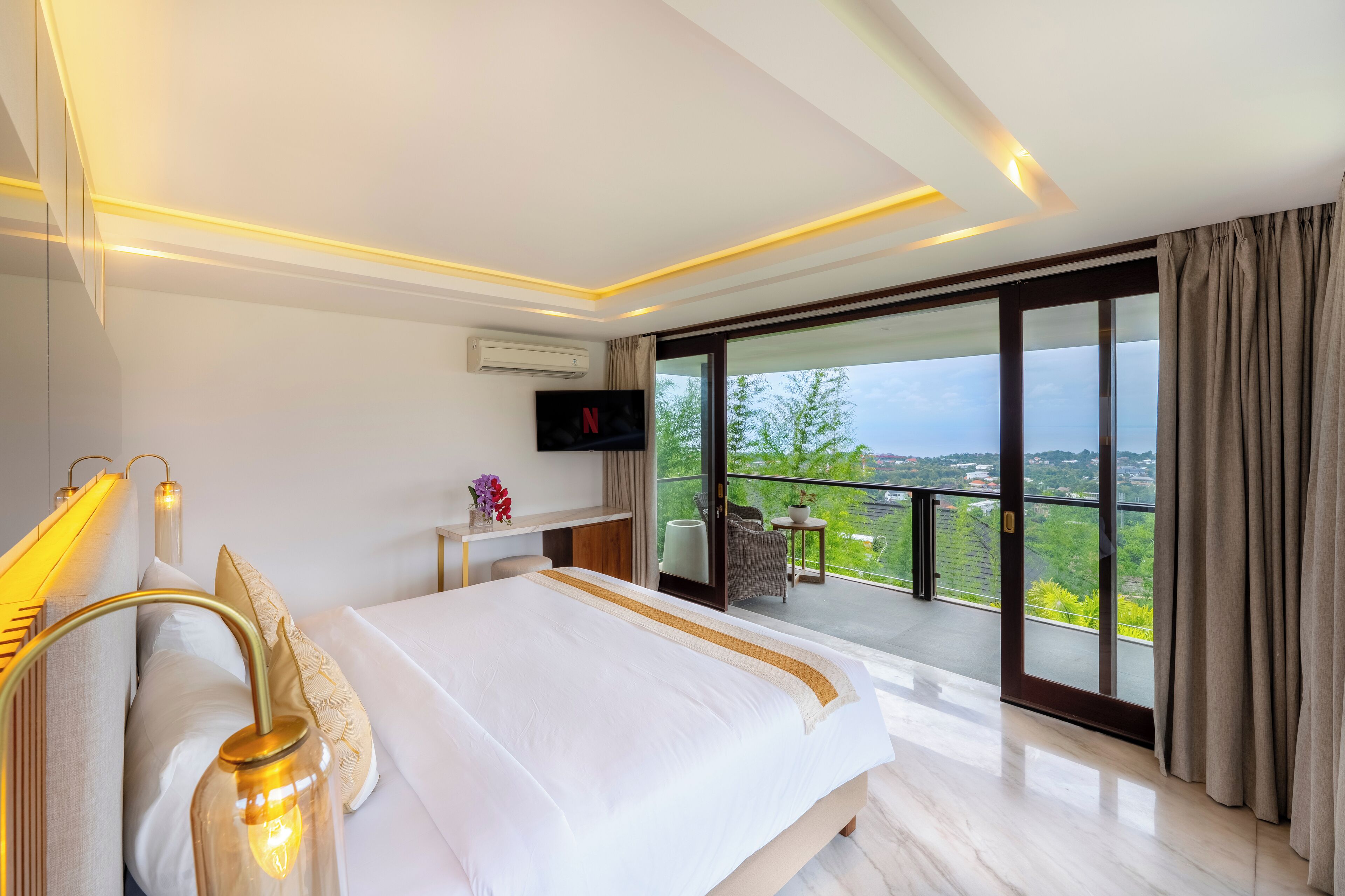 Un dormitorio de hotel moderno con una cama grande, televisión, escritorio y balcón con vistas panorámicas.