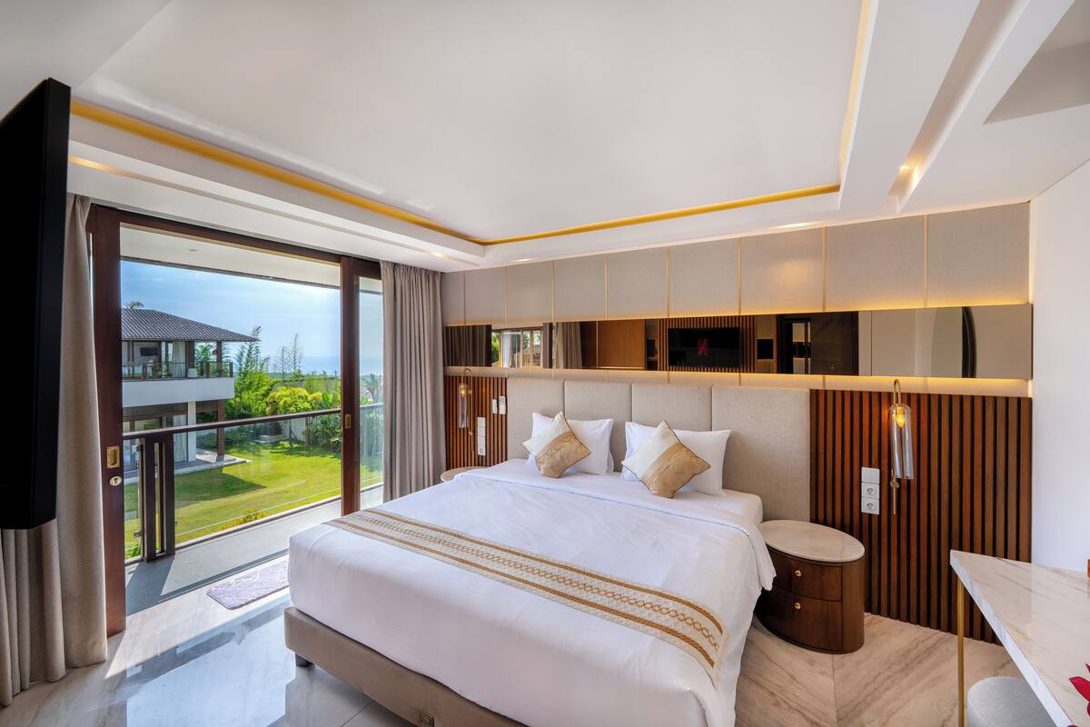 A modern hotel room with a large bed, a small bathroom, and a balcony with a view of the landscape.