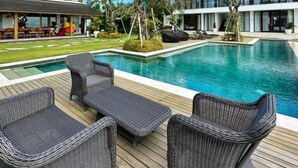Un área de piscina con sillones de mimbre, un cielo azul despejado y edificios modernos al fondo.