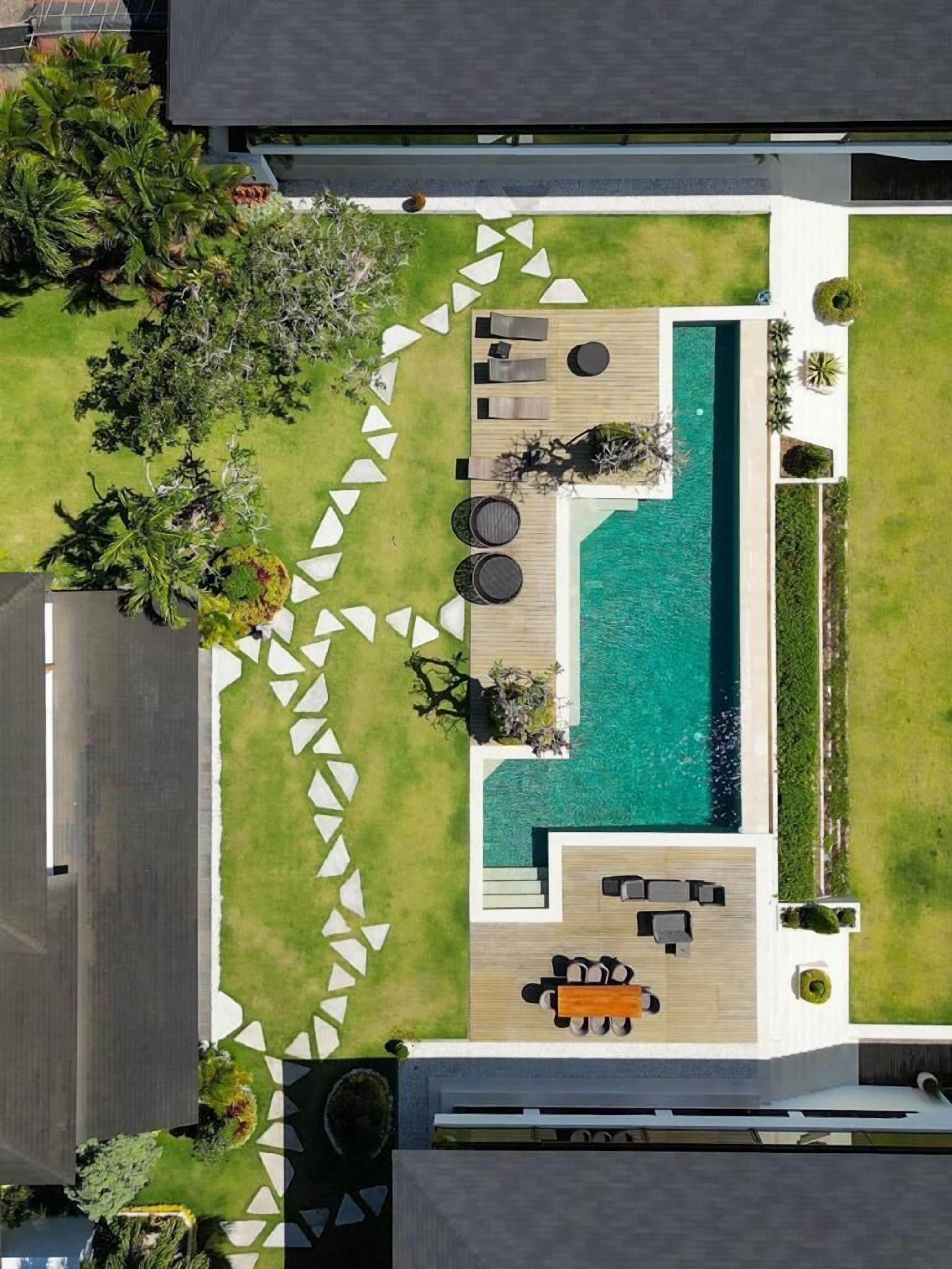 Vue aérienne d’un espace piscine extérieur moderne, avec une terrasse en bois, des chaises longues et un petit coin salon.