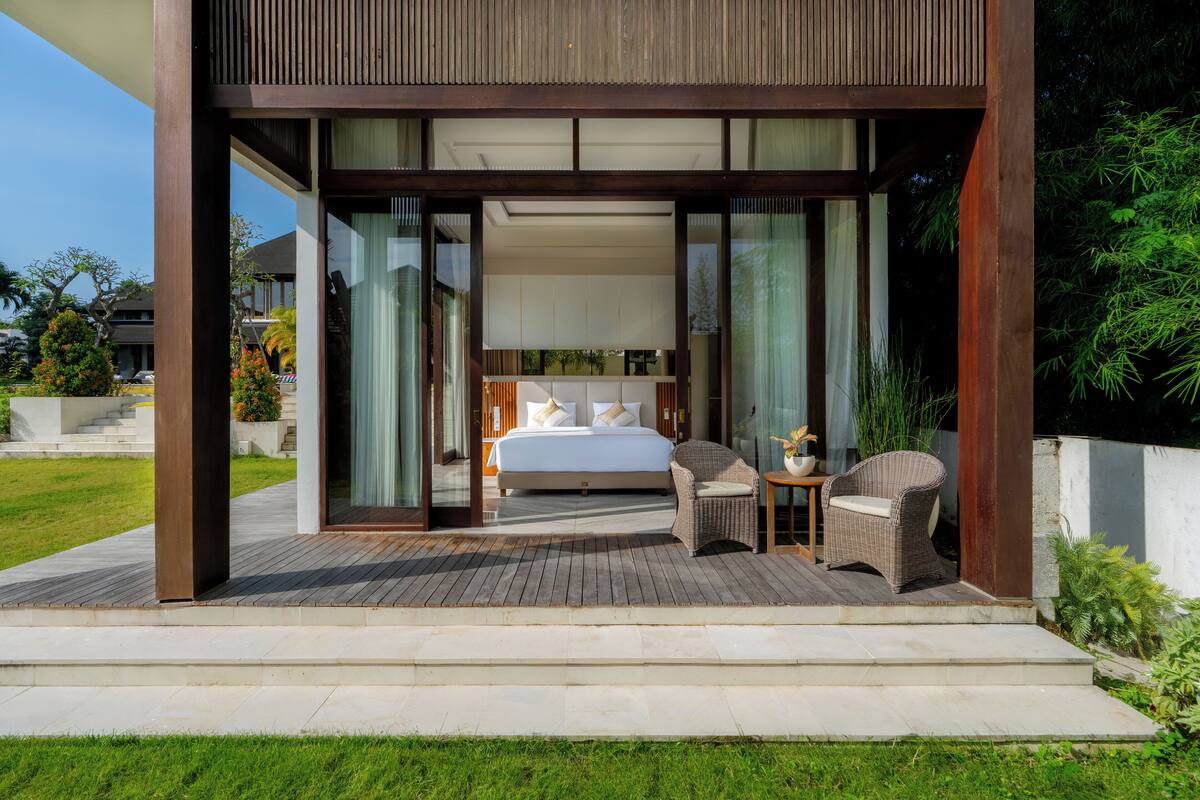 A modern bedroom with a large bed, a seating area with chairs, and a small table.