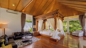 Amplia habitación con techo de madera, cama con dosel, sofá, mesa de centro y vistas al exterior con vegetación.