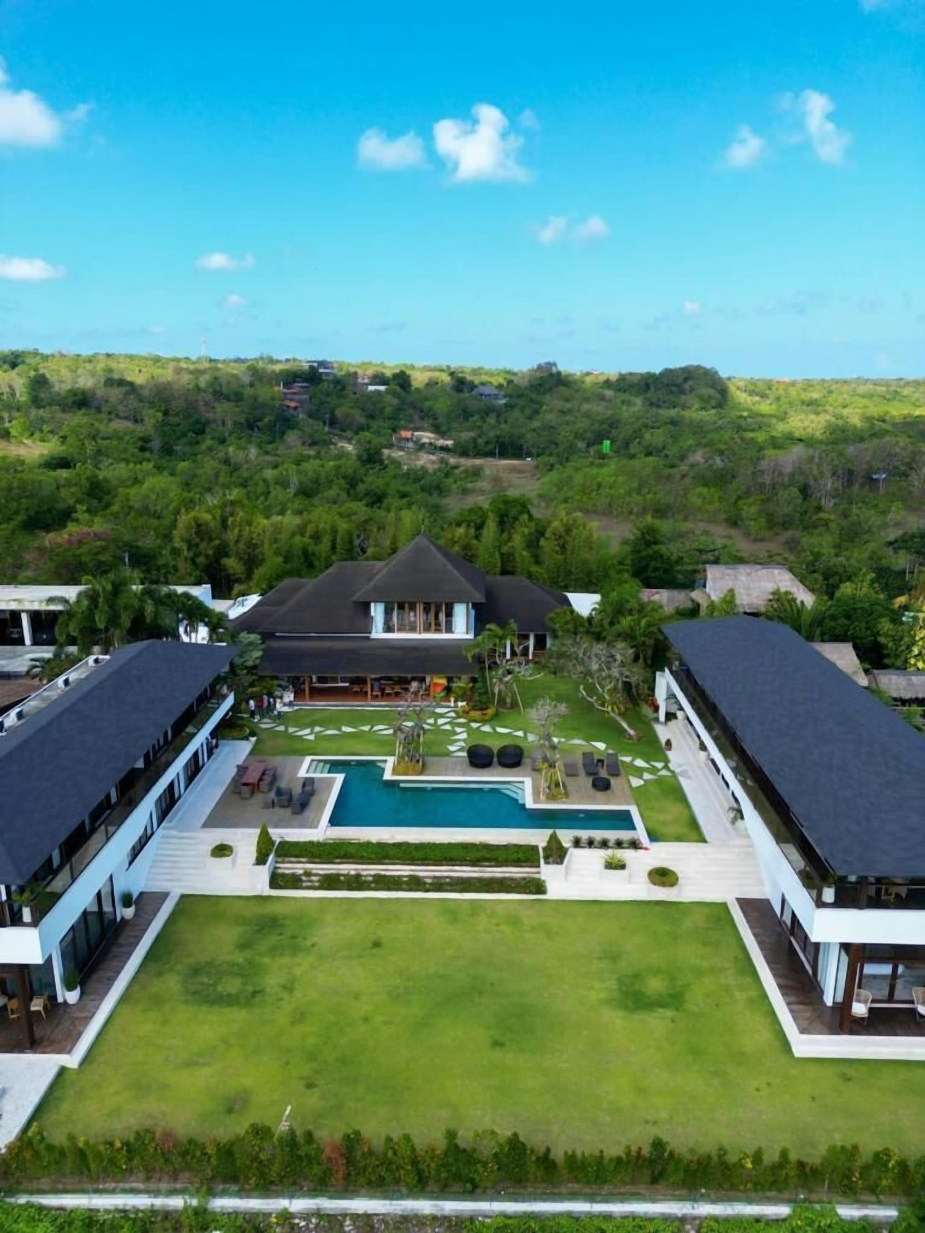 A large, modern house with a swimming pool, surrounded by lush greenery and a clear blue sky.