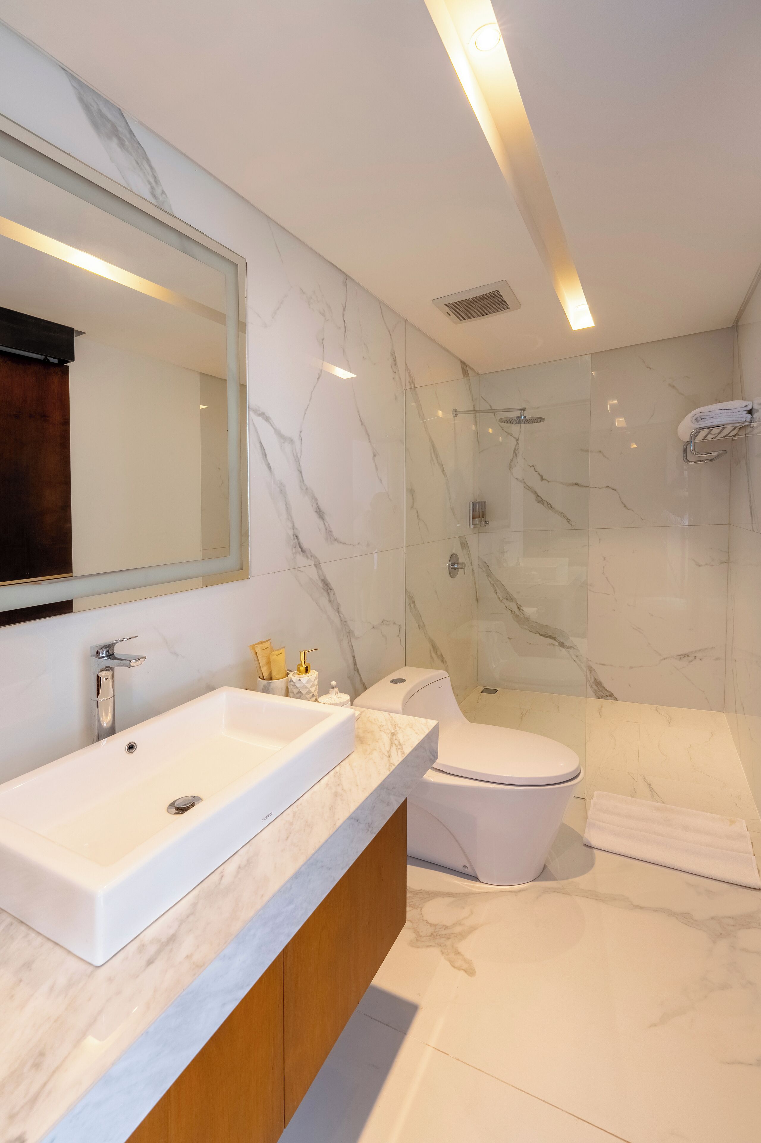 A modern bathroom with a marble vanity, a toilet, and a glass-enclosed shower.