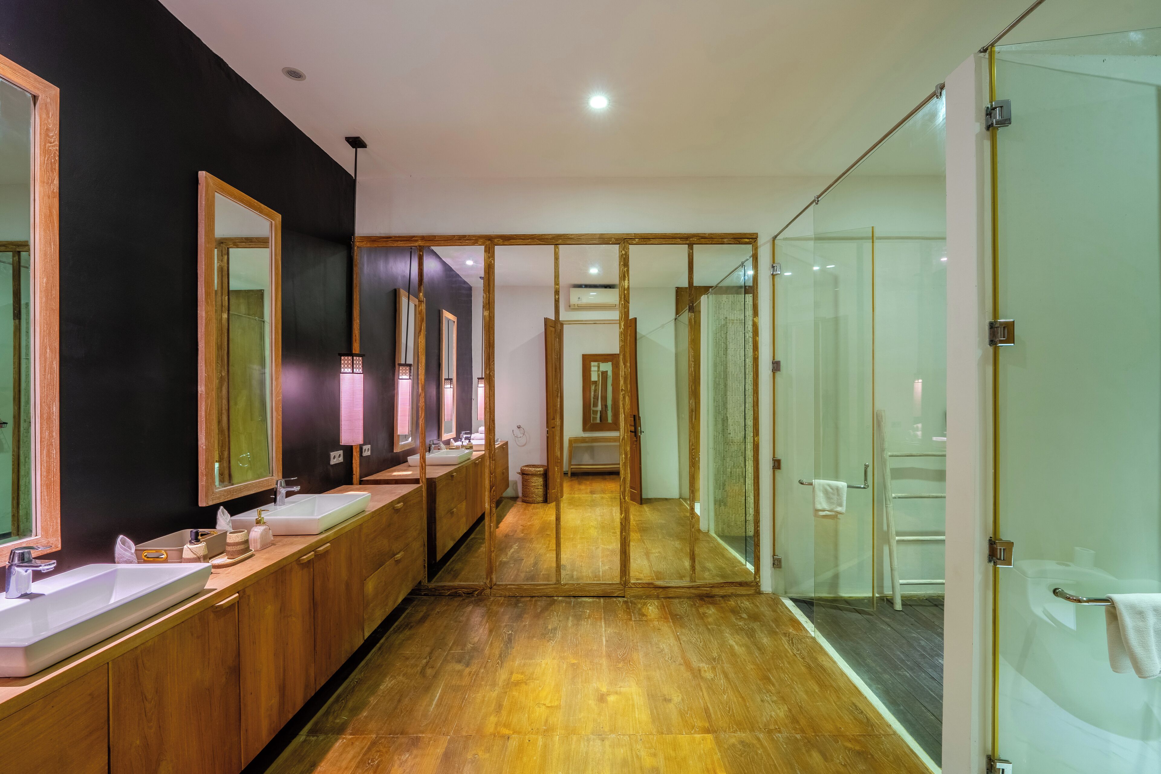 Ein modernes Badezimmer mit Holzschränken, mehreren Waschbecken und großen Spiegeln.