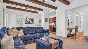 A modern living room with a blue sofa, a wooden coffee table, and a kitchen in the background.