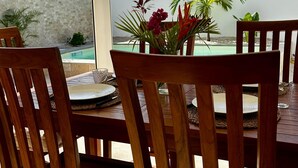 An outdoor patio with wooden chairs and a table, overlooking a swimming pool and lush greenery.