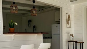 A modern kitchen with white bar stools, a central island, and hanging wicker pendant lights.